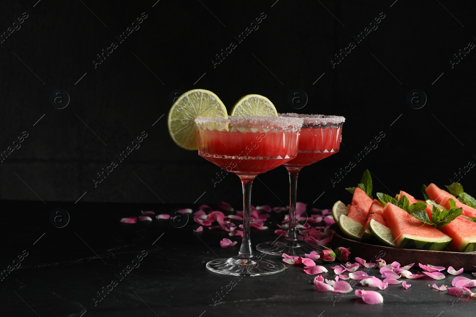 Photo of Cocktail glasses of delicious fresh watermelon juice with lime and rose petals on black table