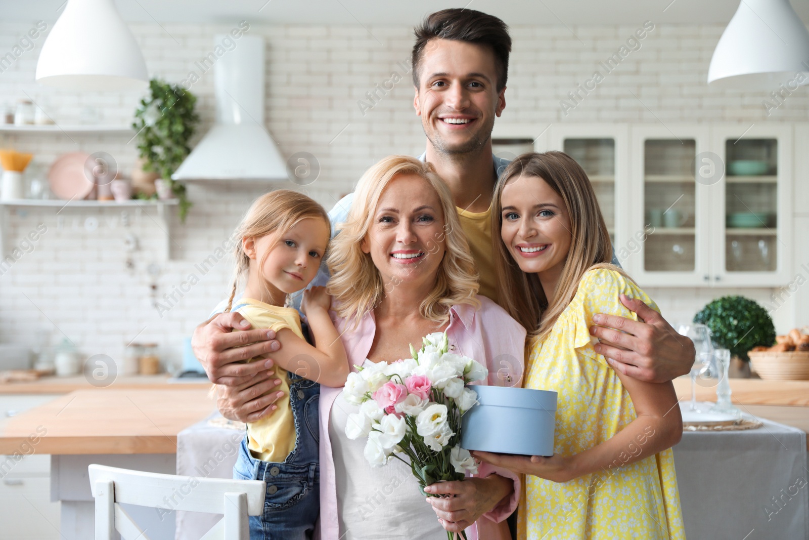 Photo of Portrait of happy family with bouquet and gift box in kitchen