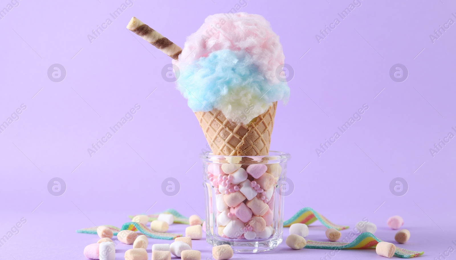 Photo of Sweet cotton candy in waffle cone and marshmallows on purple background, closeup