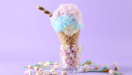 Photo of Sweet cotton candy in waffle cone and marshmallows on purple background, closeup