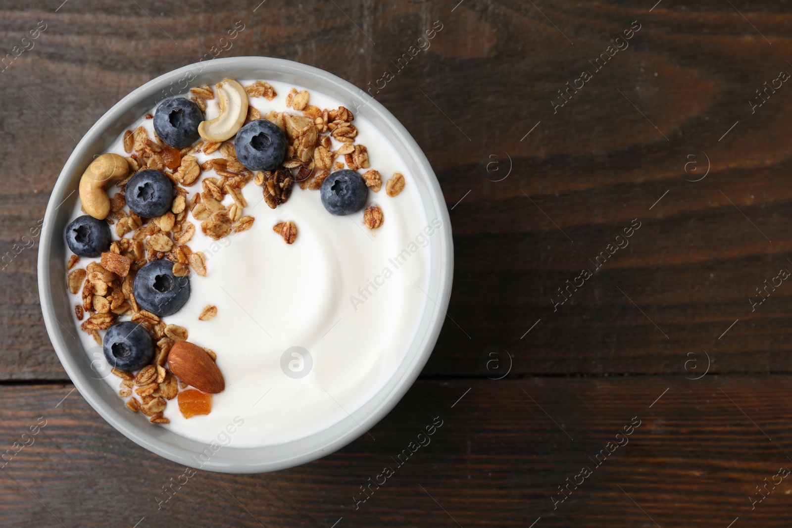 Photo of Bowl with yogurt, blueberries and granola on wooden table, top view. Space for text