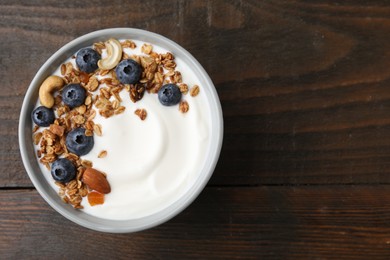 Bowl with yogurt, blueberries and granola on wooden table, top view. Space for text