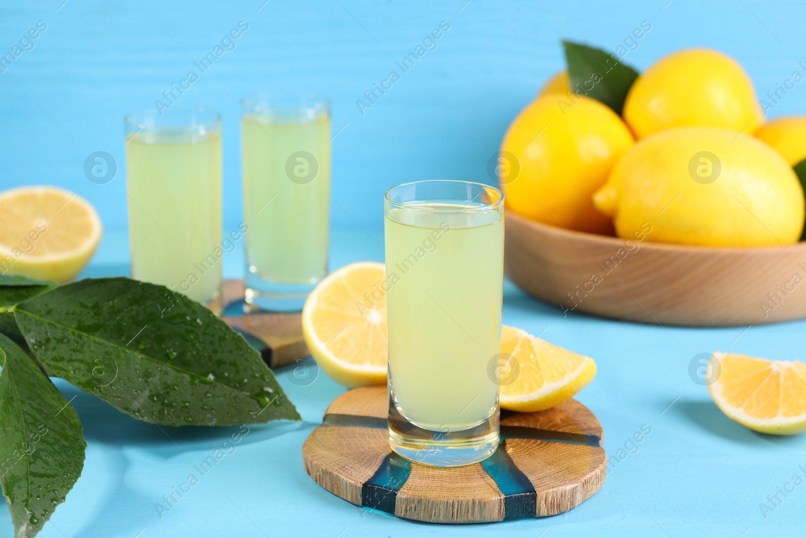 Photo of Tasty limoncello liqueur, lemons and green leaves on light blue table