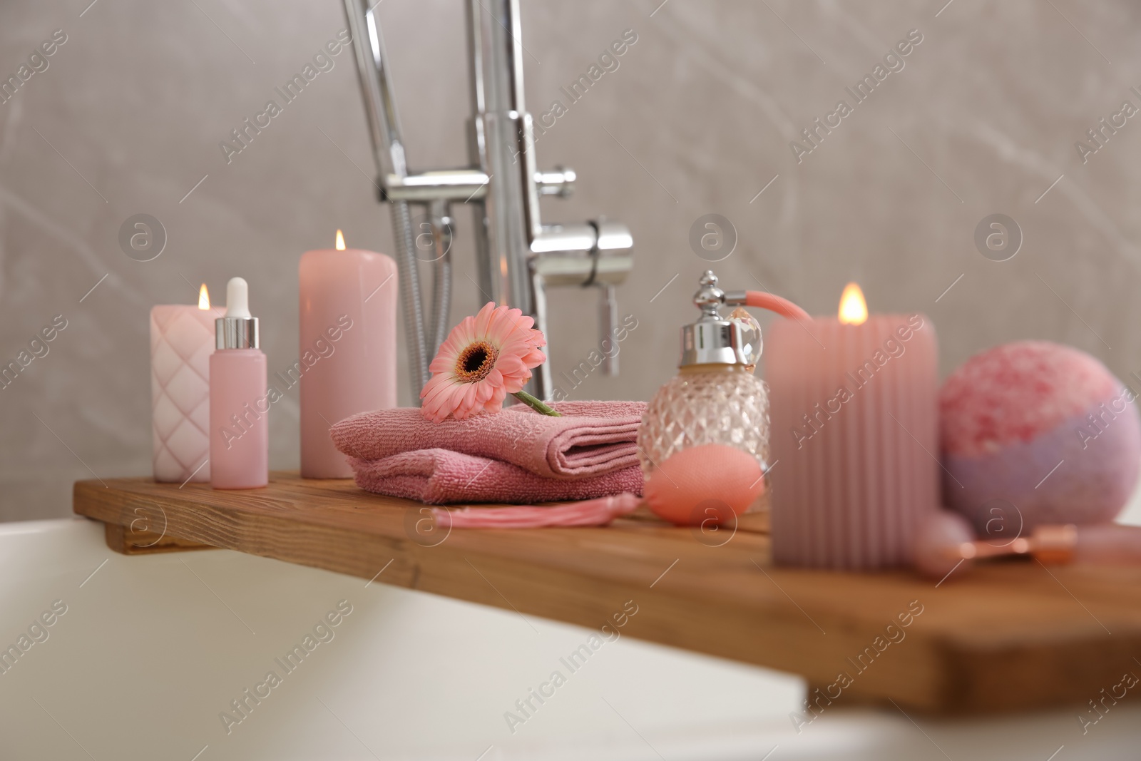 Photo of Wooden bath tray with candles and personal care products on tub, closeup