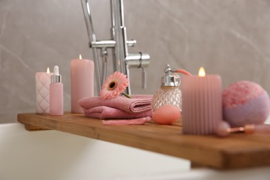 Photo of Wooden bath tray with candles and personal care products on tub, closeup