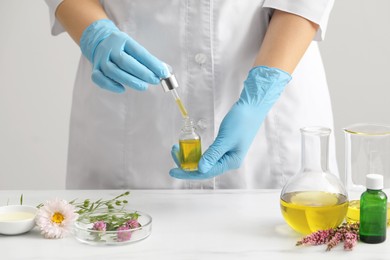 Scientist developing cosmetic oil at white table, closeup