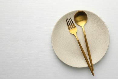 Clean plate, fork and spoon on white table, top view. Space for text