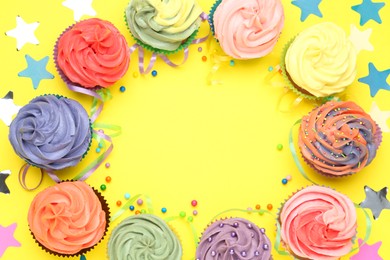 Photo of Delicious cupcakes with bright cream and party decor on yellow background, flat lay. Space for text