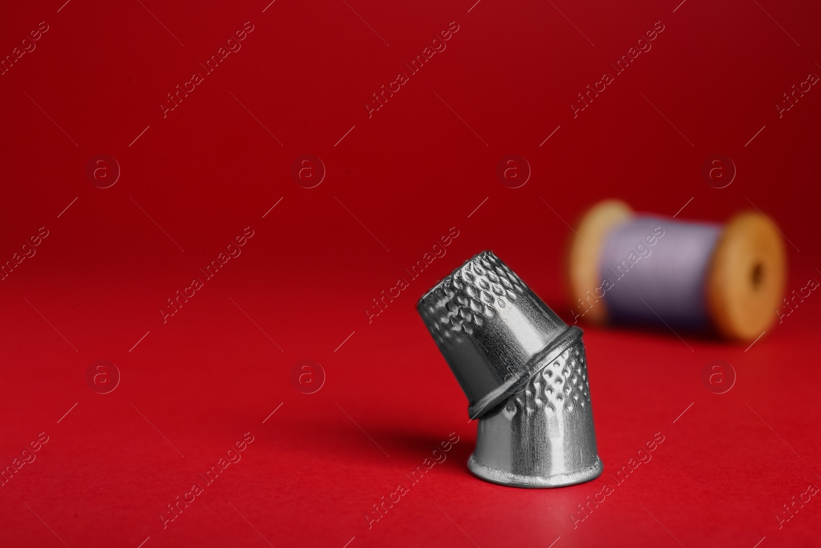 Photo of Silver thimbles on red background, space for text. Sewing accessories