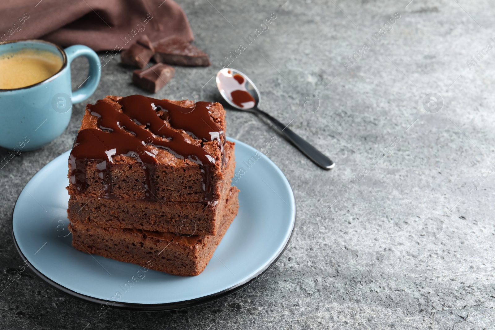 Photo of Delicious chocolate brownies with sweet syrup served on grey table. Space for text
