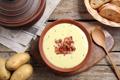 Photo of Tasty potato soup with bacon and rosemary in bowl served on wooden table, flat lay