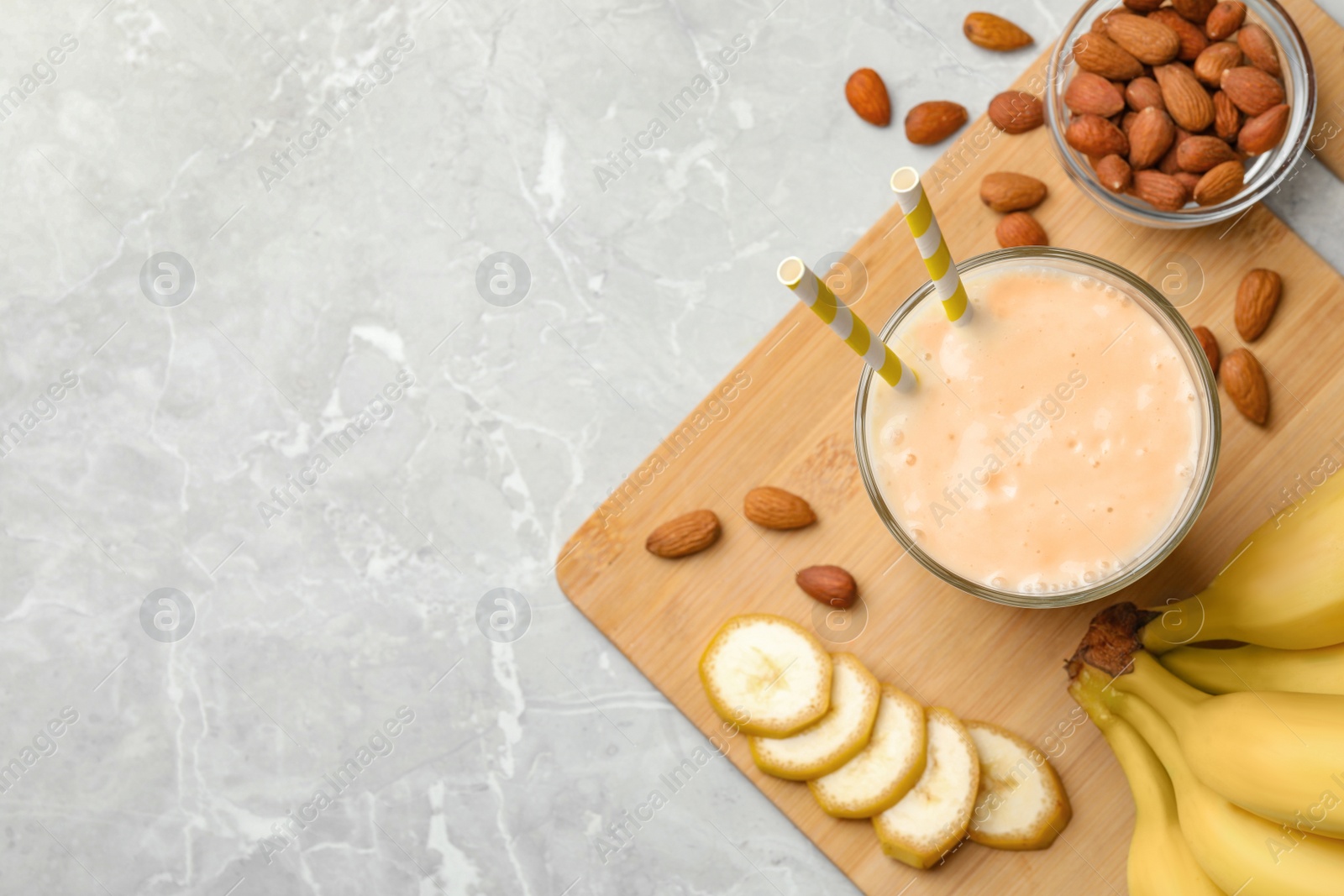 Photo of Flat lay composition of banana smoothie in glass and nuts on light grey marble table. Space for text