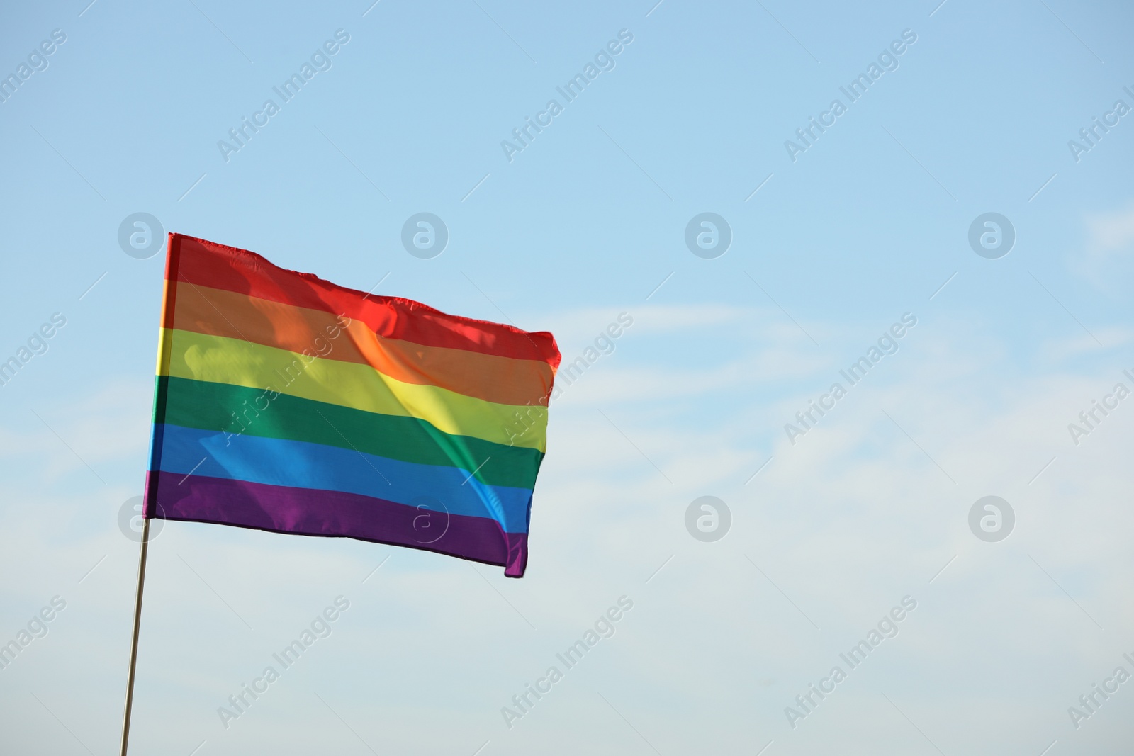 Photo of Bright LGBT flag against blue sky with clouds, space for text