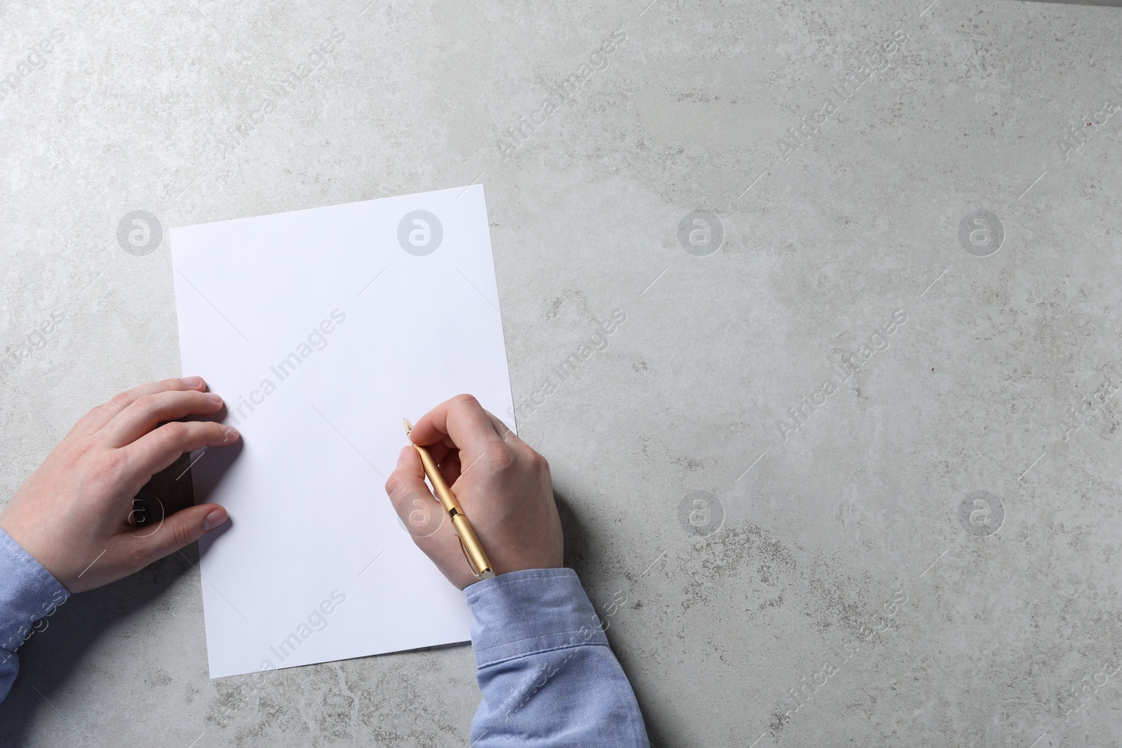 Photo of Man writing on sheet of paper with pen at light grey table, top view. Space for text