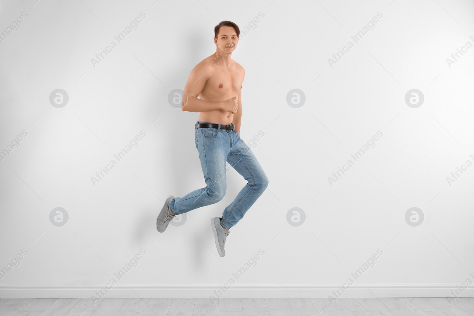 Photo of Young man in stylish jeans jumping near white wall