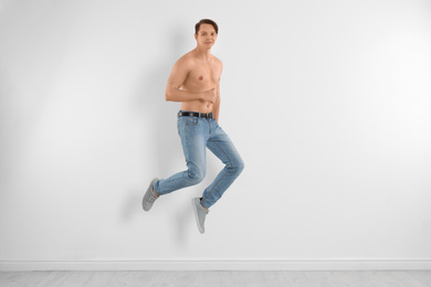 Young man in stylish jeans jumping near white wall