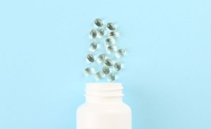 Photo of Bottle and vitamin capsules on light blue background, top view