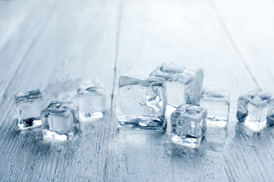 Photo of Crystal clear ice cubes with water drops on white wooden table