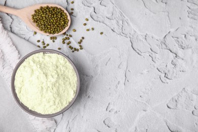 Photo of Mung bean flour in bowl and seeds on white textured table, flat lay. Space for text