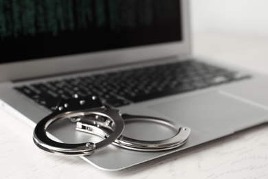Photo of Laptop and handcuffs on white wooden table, closeup. Cyber crime