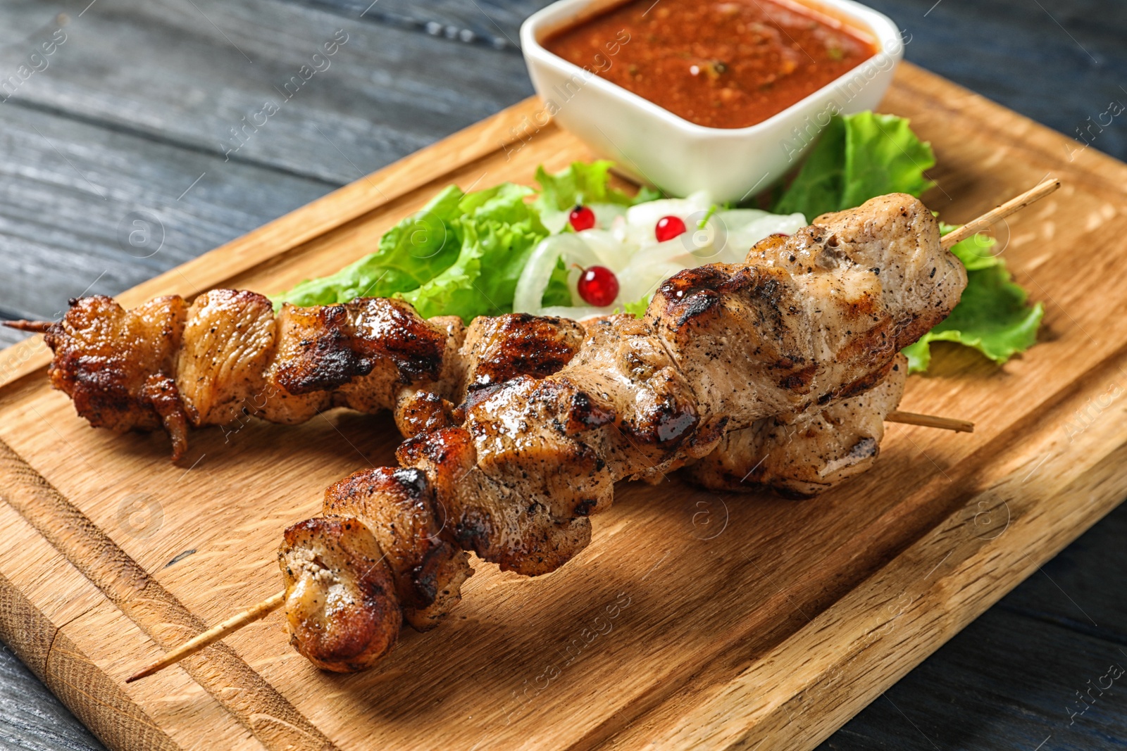 Photo of Wooden board with juicy shish kebab, closeup