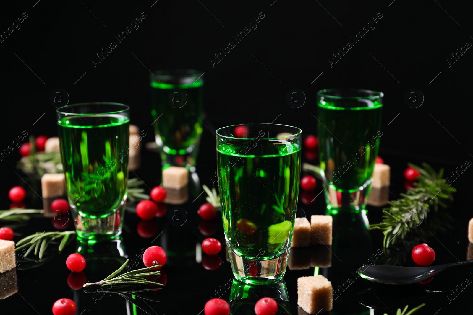 Photo of Absinthe in shot glasses, cranberries, rosemary and brown sugar on mirror table. Alcoholic drink