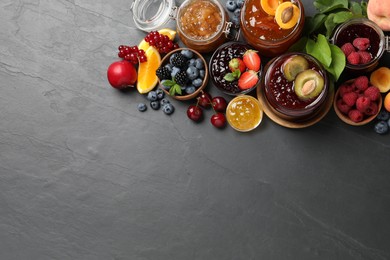 Jars with different jams and fresh fruits on black table, flat lay. Space for text