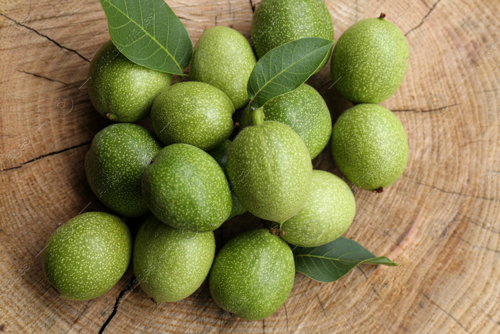 Photo of Many green walnuts and leaves on wooden stump, flat lay