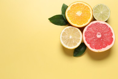 Different cut citrus fruits and leaves on yellow table, flat lay. Space for text