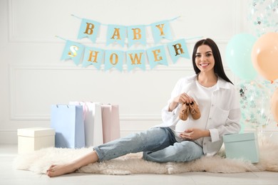 Happy pregnant woman with small booties in room decorated for baby shower party
