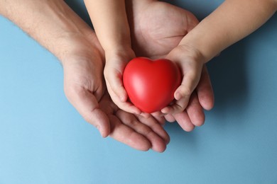 Photo of Father and his child holding red decorative heart on light blue background, top view