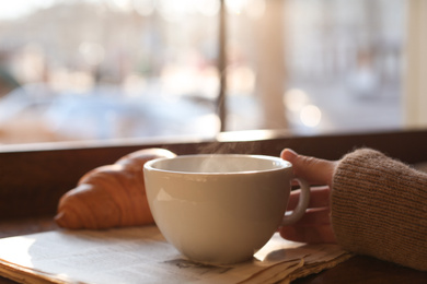 Woman with cup of delicious morning coffee near window indoors