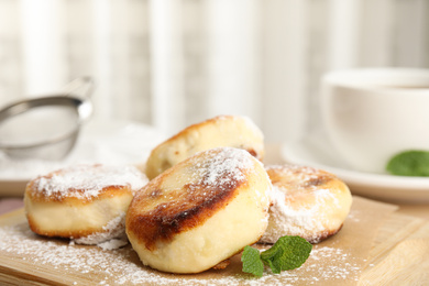 Delicious cottage cheese pancakes with sugar powder on wooden board, closeup