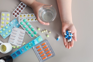 Photo of Little child with many different pills and water at table, top view. Danger of medicament intoxication