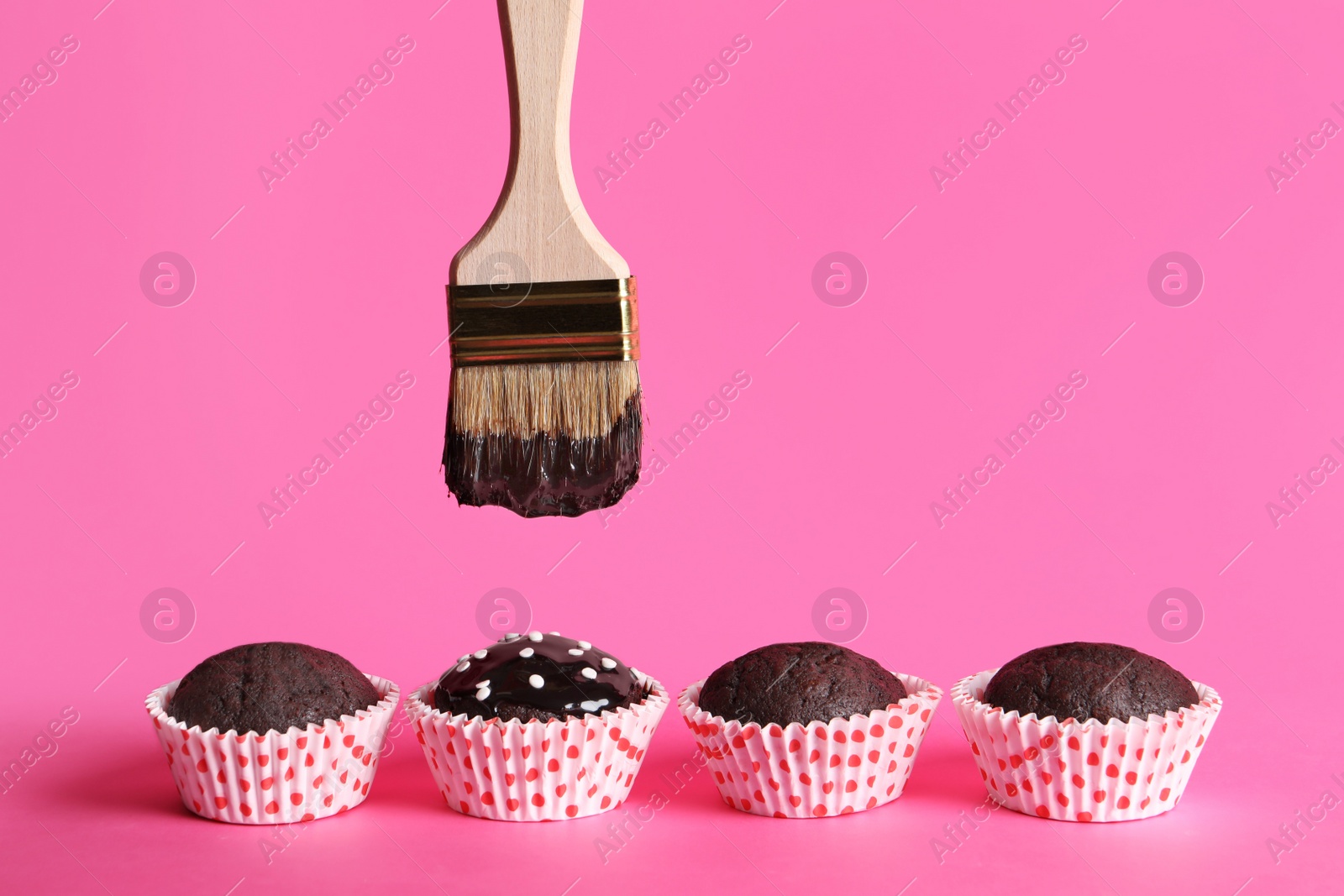 Photo of Spreading glaze onto chocolate muffins with brush on pink background