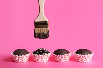 Photo of Spreading glaze onto chocolate muffins with brush on pink background