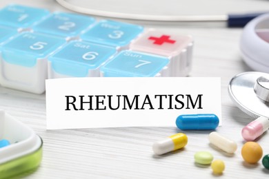 Photo of Card with word Rheumatism and pills on white wooden table