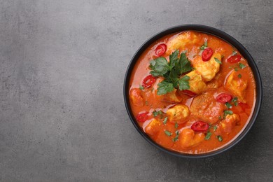 Bowl of delicious chicken curry on grey table, top view. Space for text