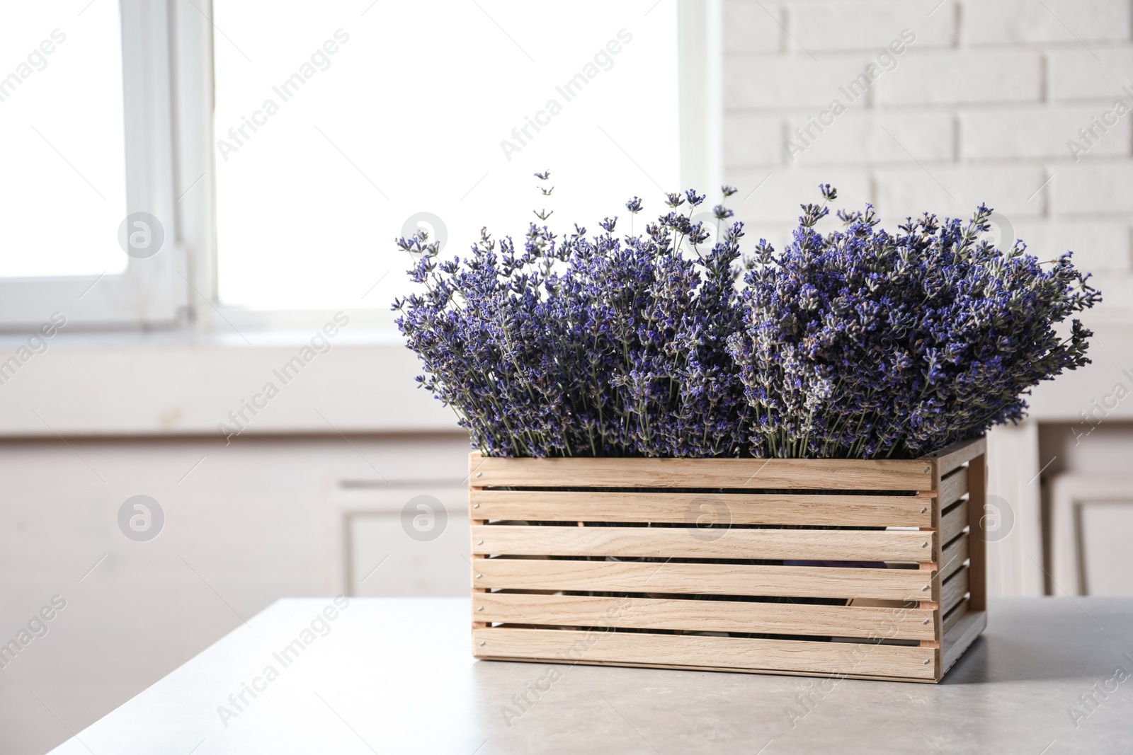 Photo of Fresh lavender flowers in wooden crate on stone table indoors, space for text