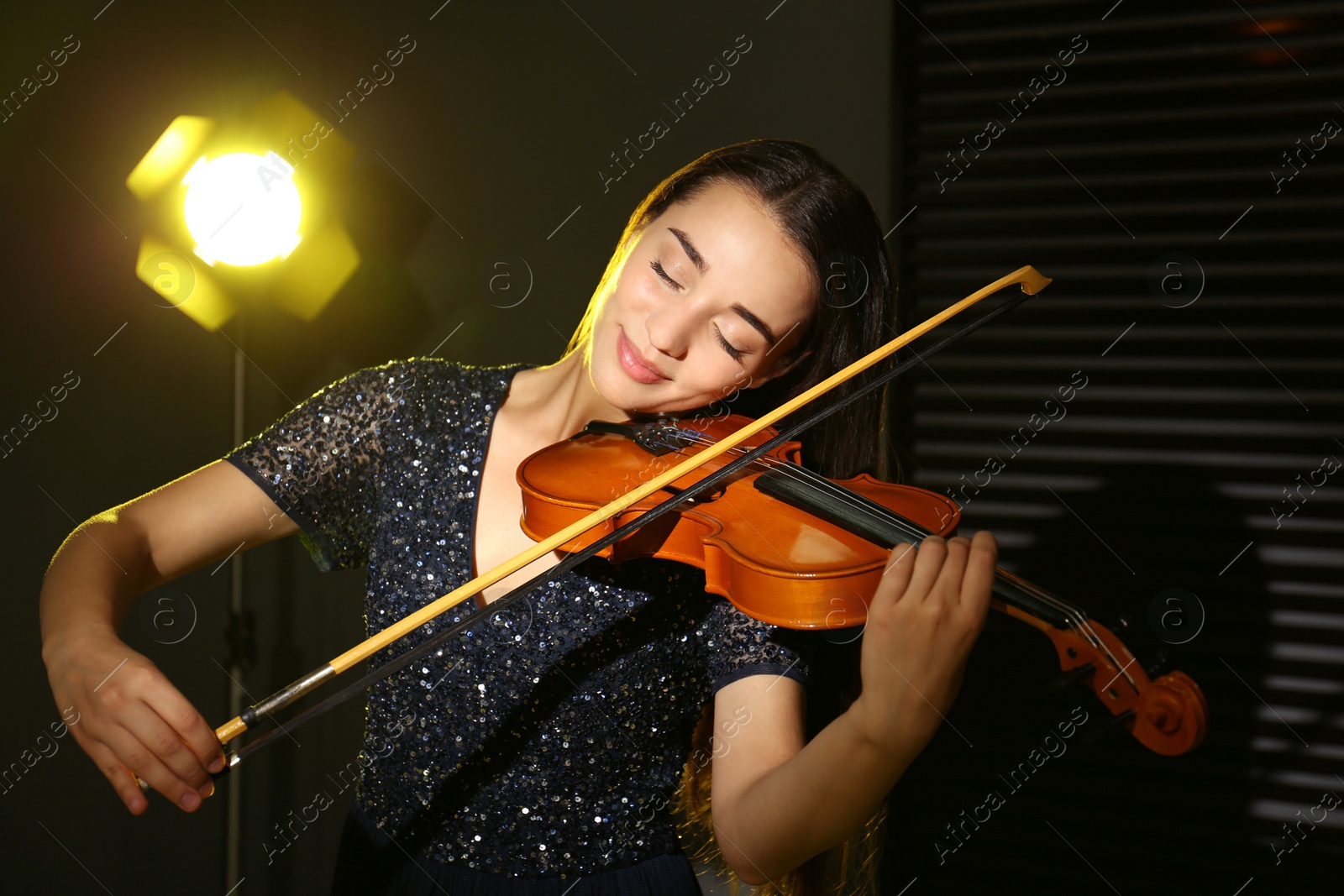 Photo of Beautiful young woman playing violin in dark room