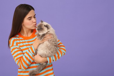 Photo of Woman kissing her cute cat on purple background, space for text