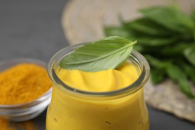 Photo of Jar with tasty curry sauce and basil leaf, closeup