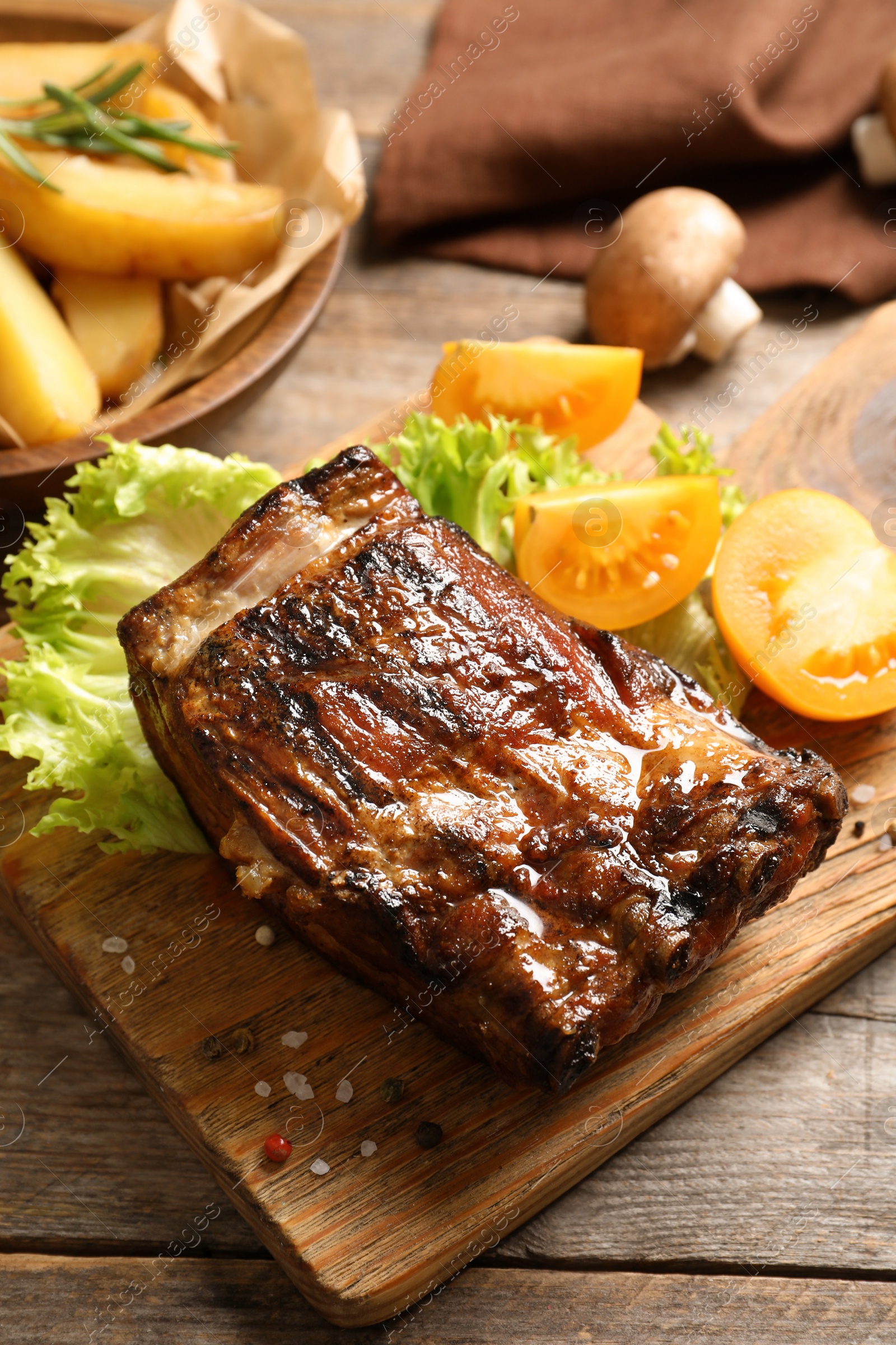 Photo of Delicious barbecued ribs served with garnish on wooden board