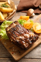 Photo of Delicious barbecued ribs served with garnish on wooden board