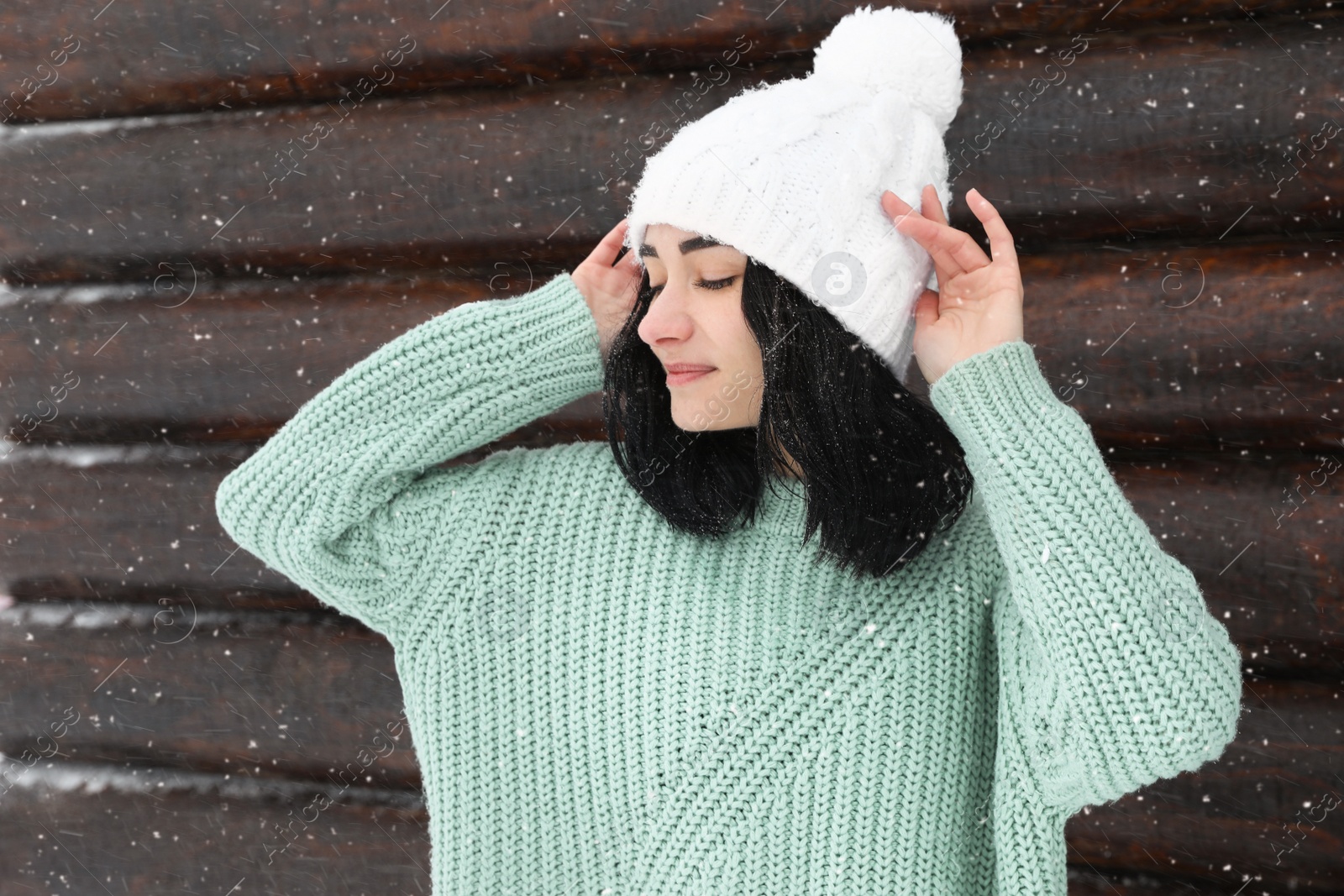 Photo of Young woman wearing warm sweater and hat near wooden wall. Winter season