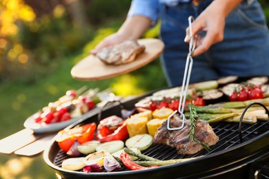 Woman cooking meat and vegetables on barbecue grill outdoors, closeup