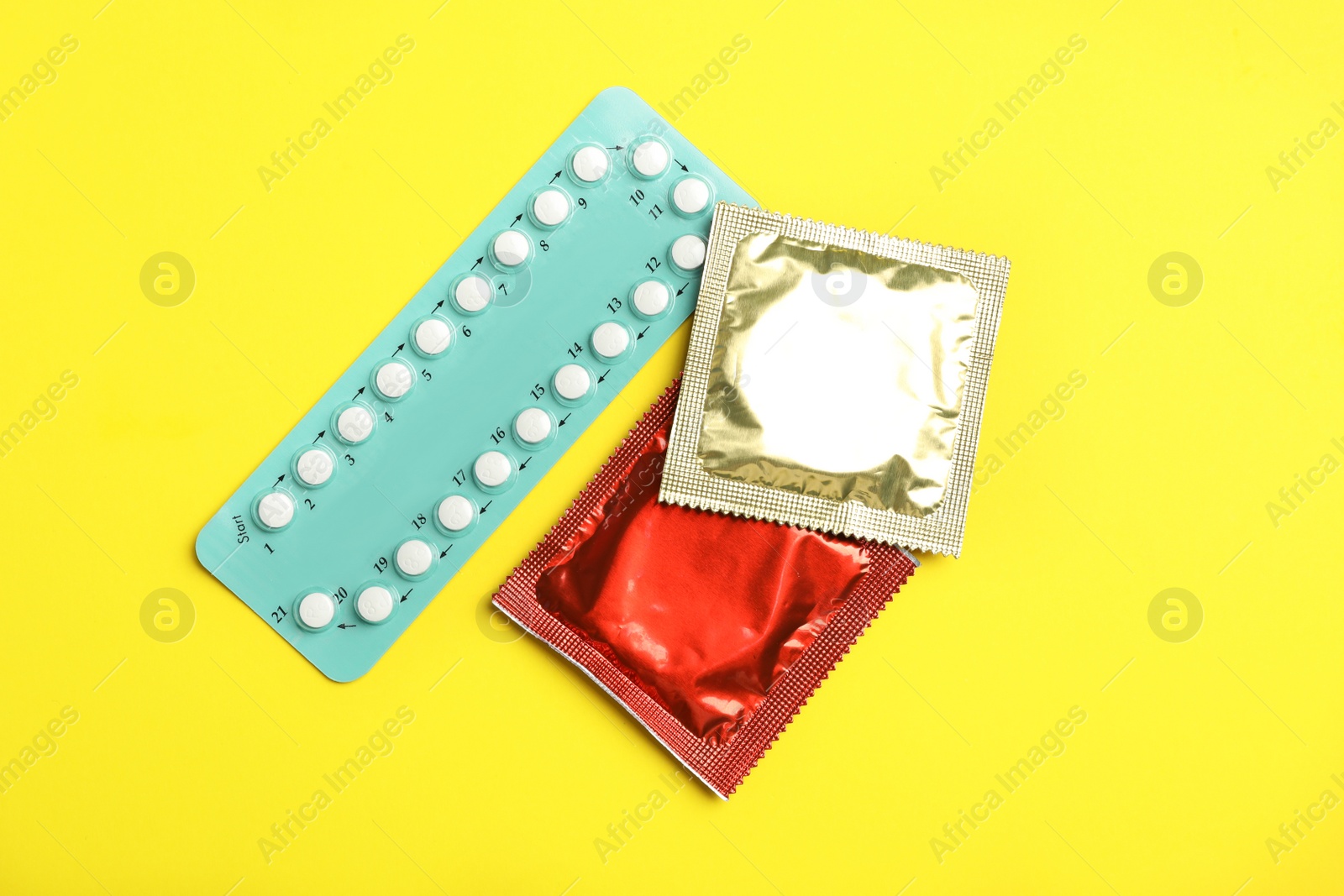 Photo of Condoms and birth control pills on yellow background, flat lay. Safe sex concept