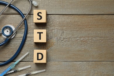 Photo of Abbreviation STD made with cubes, syringes and stethoscope on wooden table, flat lay. Space for text