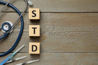 Abbreviation STD made with cubes, syringes and stethoscope on wooden table, flat lay. Space for text