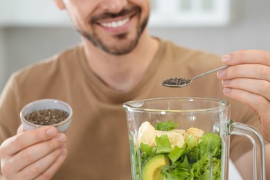 Photo of Man adding chia seeds into blender with ingredients for smoothie indoors, closeup